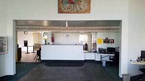 A reception area with a counter, a clock, a lamp, and a poster on the wall. - Simple Rewards Inn (Guymon)