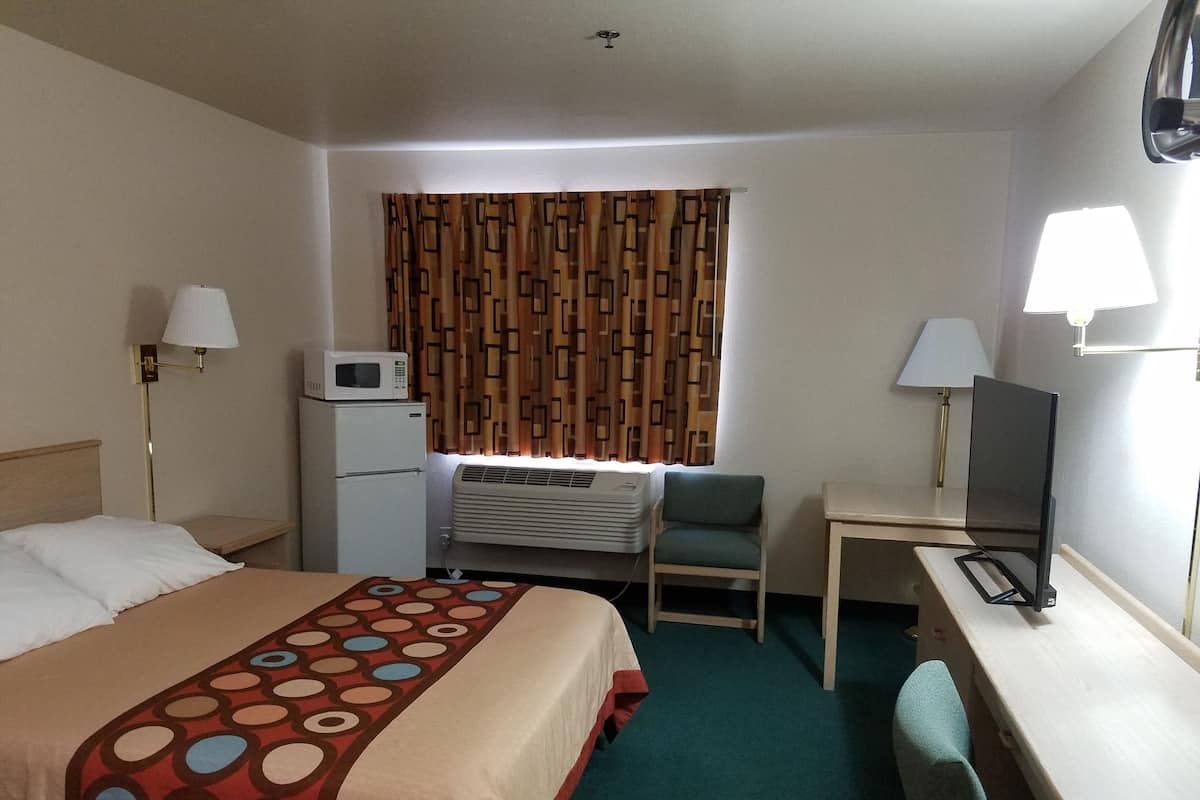 Quarto de hotel com cama, escrivaninha, cadeira, ar condicionado, micro-ondas e duas luminárias.