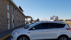 A white SUV parked in front of a building with a brick facade and large windows. - Simple Rewards Inn (Guymon)