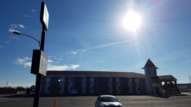 A parking lot with a building in the background, a street sign, and a clear blue sky.
