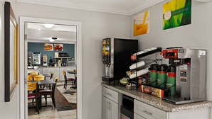 Une cuisine équipée d’une machine à café, d’un réfrigérateur et d’un coin repas avec des chaises et une table.