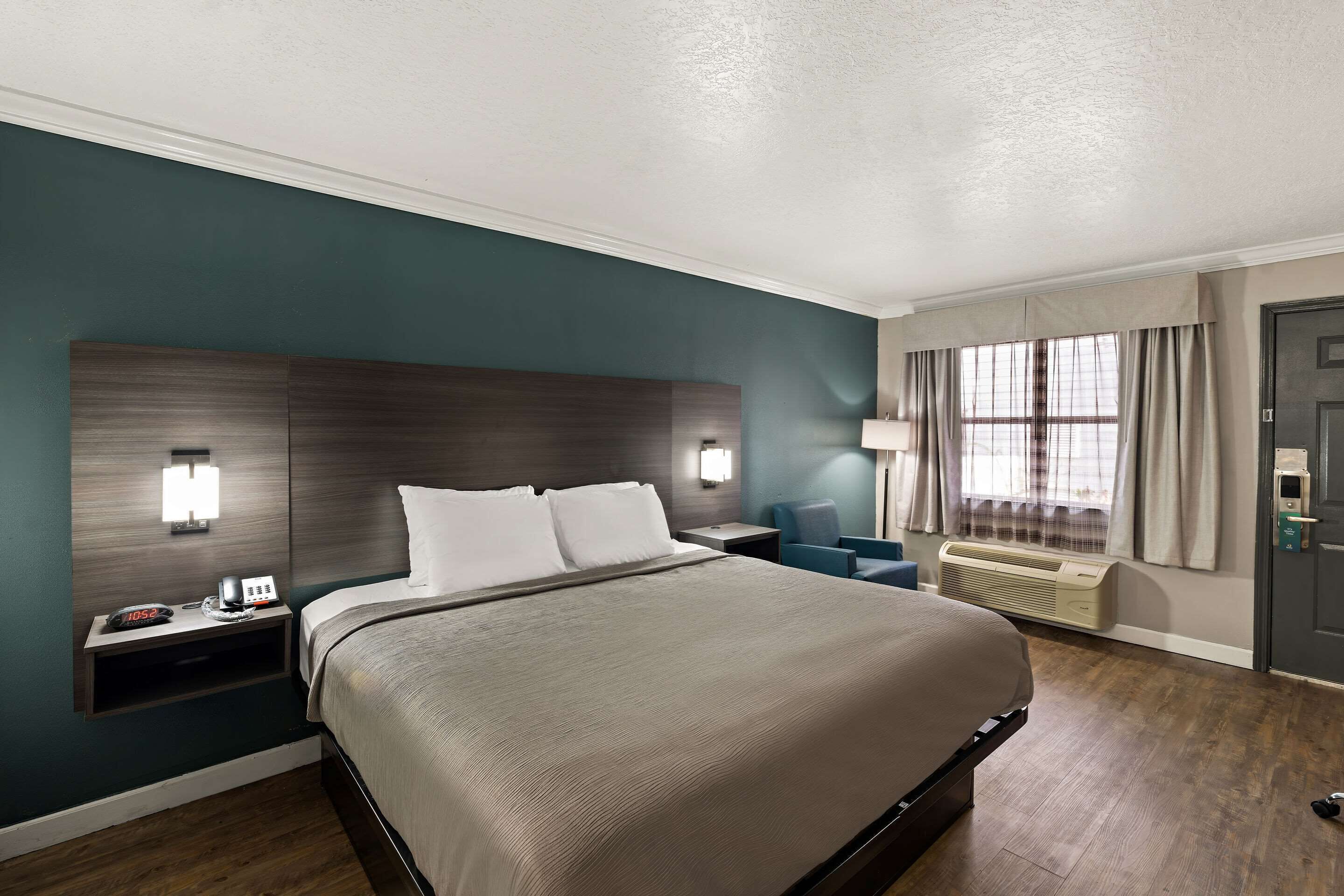 Habitación de hotel con una cama grande, mesitas de noche, un escritorio, una silla, una ventana con cortinas y un equipo de aire acondicionado.