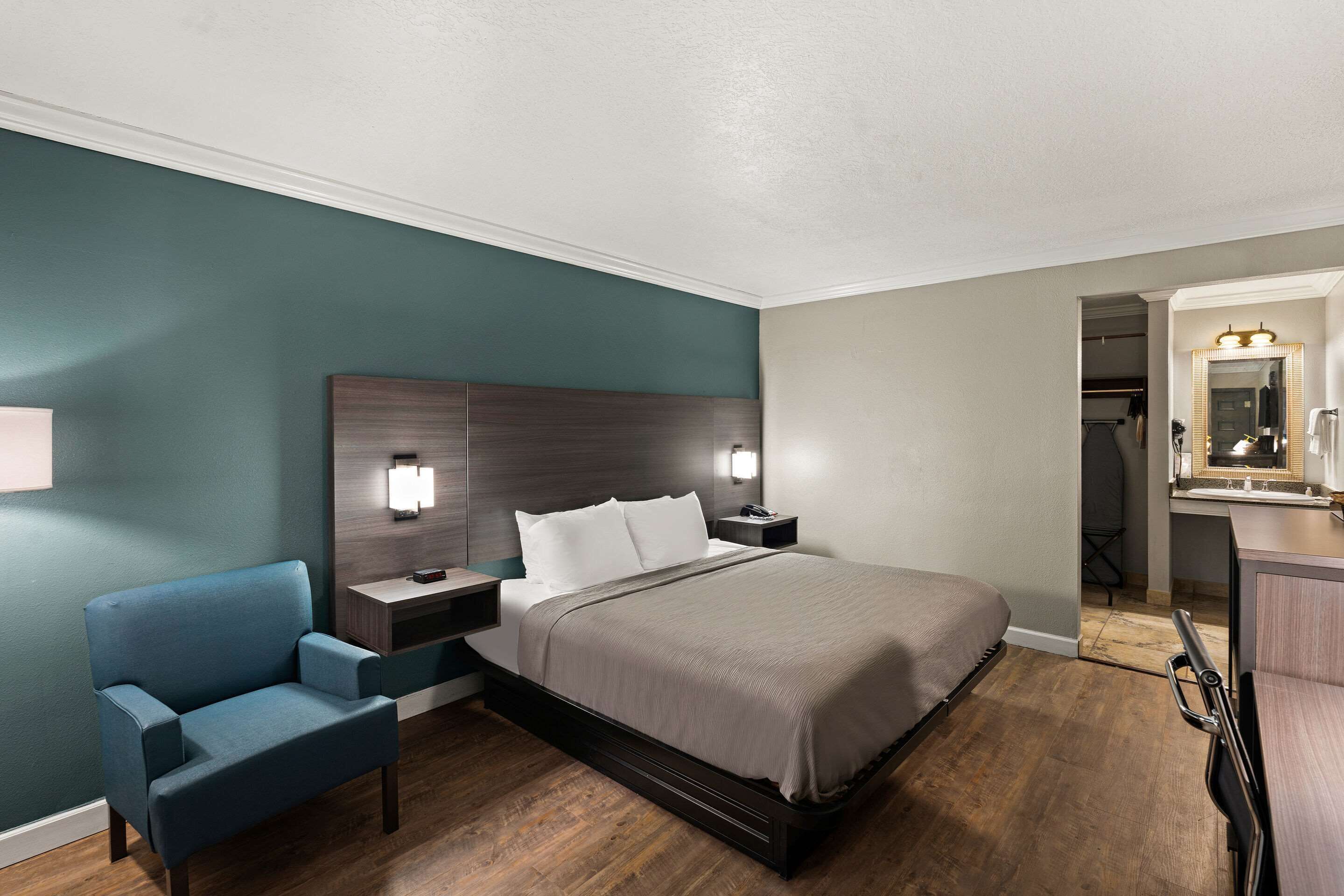 Una habitación de hotel moderna con una cama grande, una mesita de noche, una silla y un escritorio con un espejo.