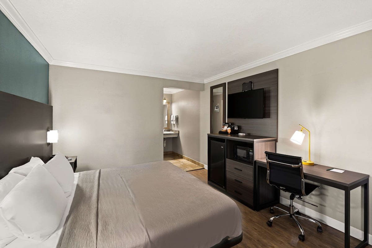 Een hotelkamer met een bed, bureau, stoel en een televisie aan de muur.