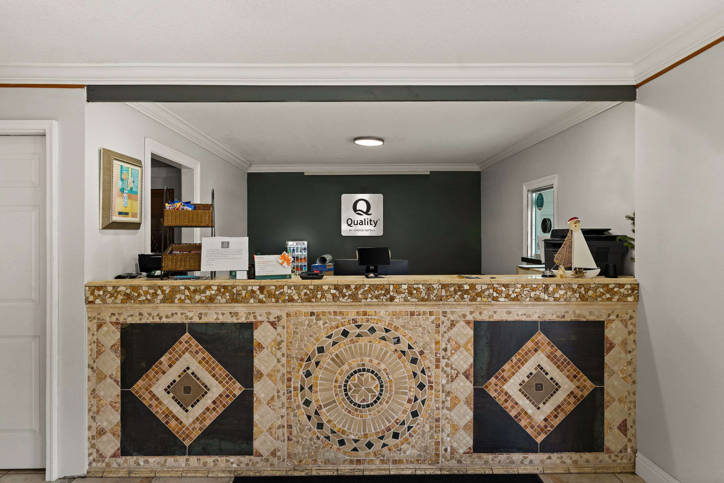 A reception desk with a mosaic tile design, a sign reading "Quality by Choice Hotel", and a small decorative figure on the right.