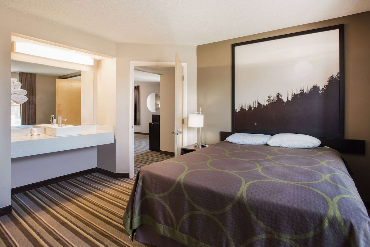 A hotel room with a bed, a bathroom with a sink and mirror, and a large painting on the wall.