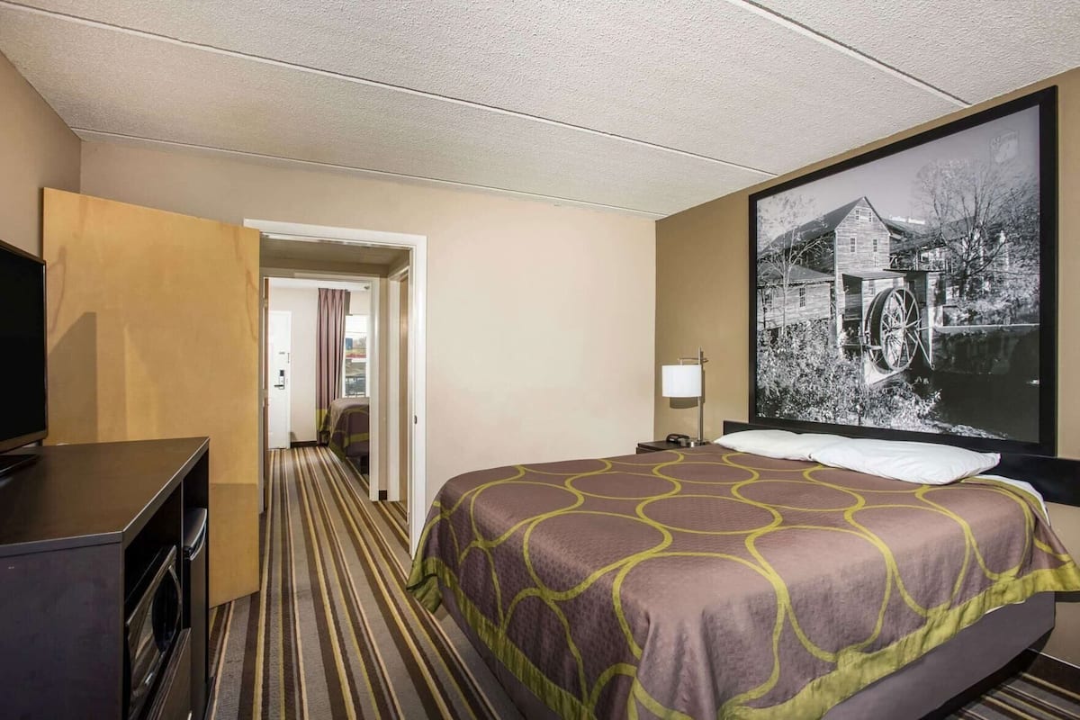 A hotel room with a bed, a television, a desk, and a large framed picture on the wall.