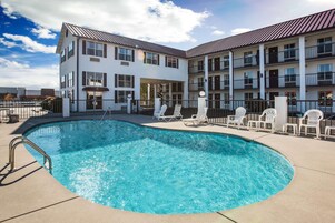 A hotel with a swimming pool, outdoor seating, and a multi-story building with balconies.