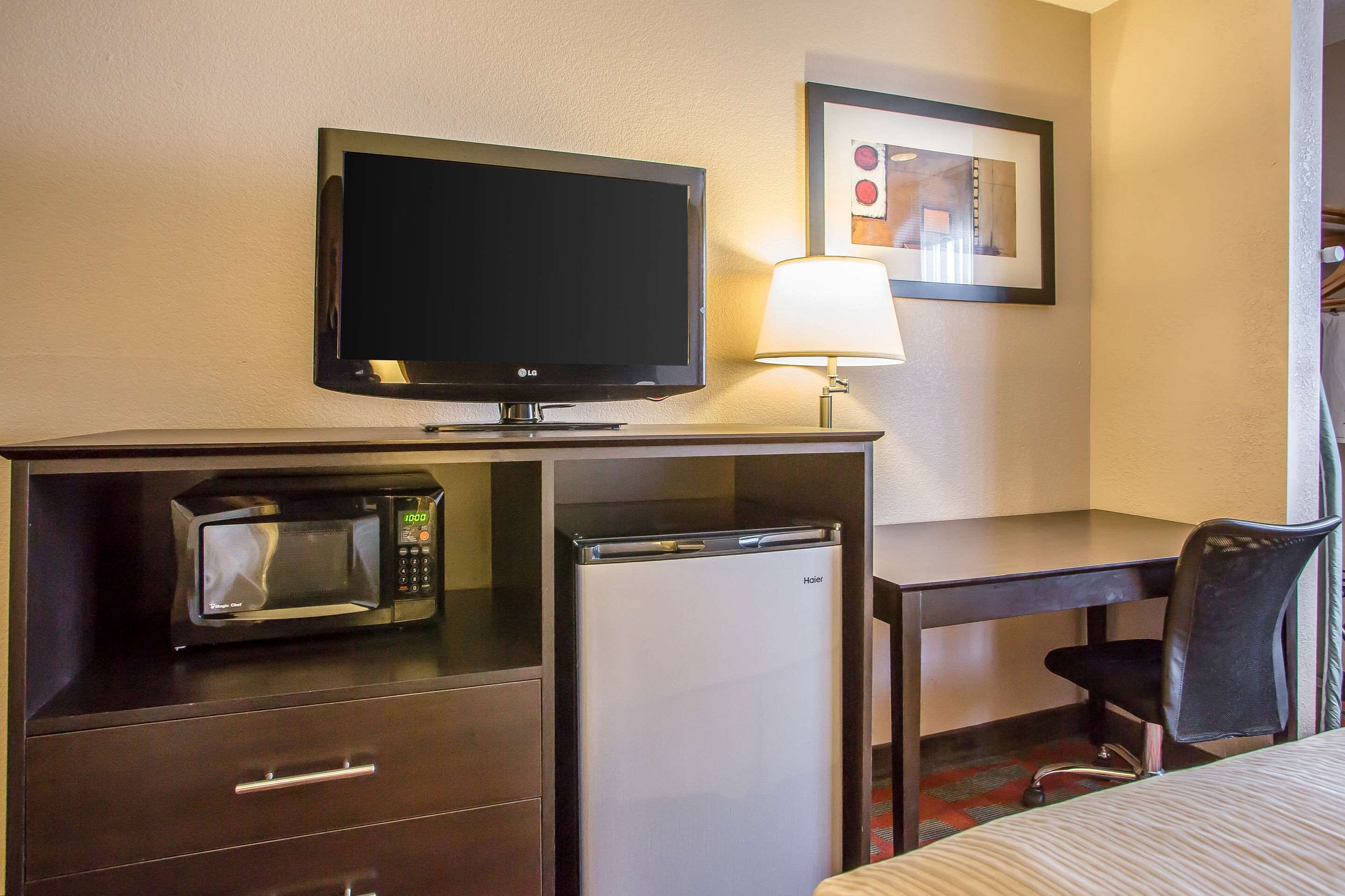 Habitación de hotel con televisión de pantalla plana, microondas, mini refrigerador, escritorio, silla y cama.