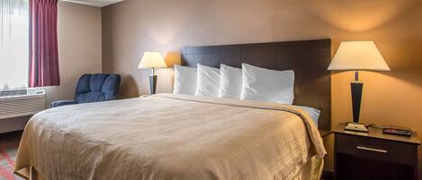 A hotel room with a large bed, two bedside lamps, a chair, and a nightstand with a remote control.
