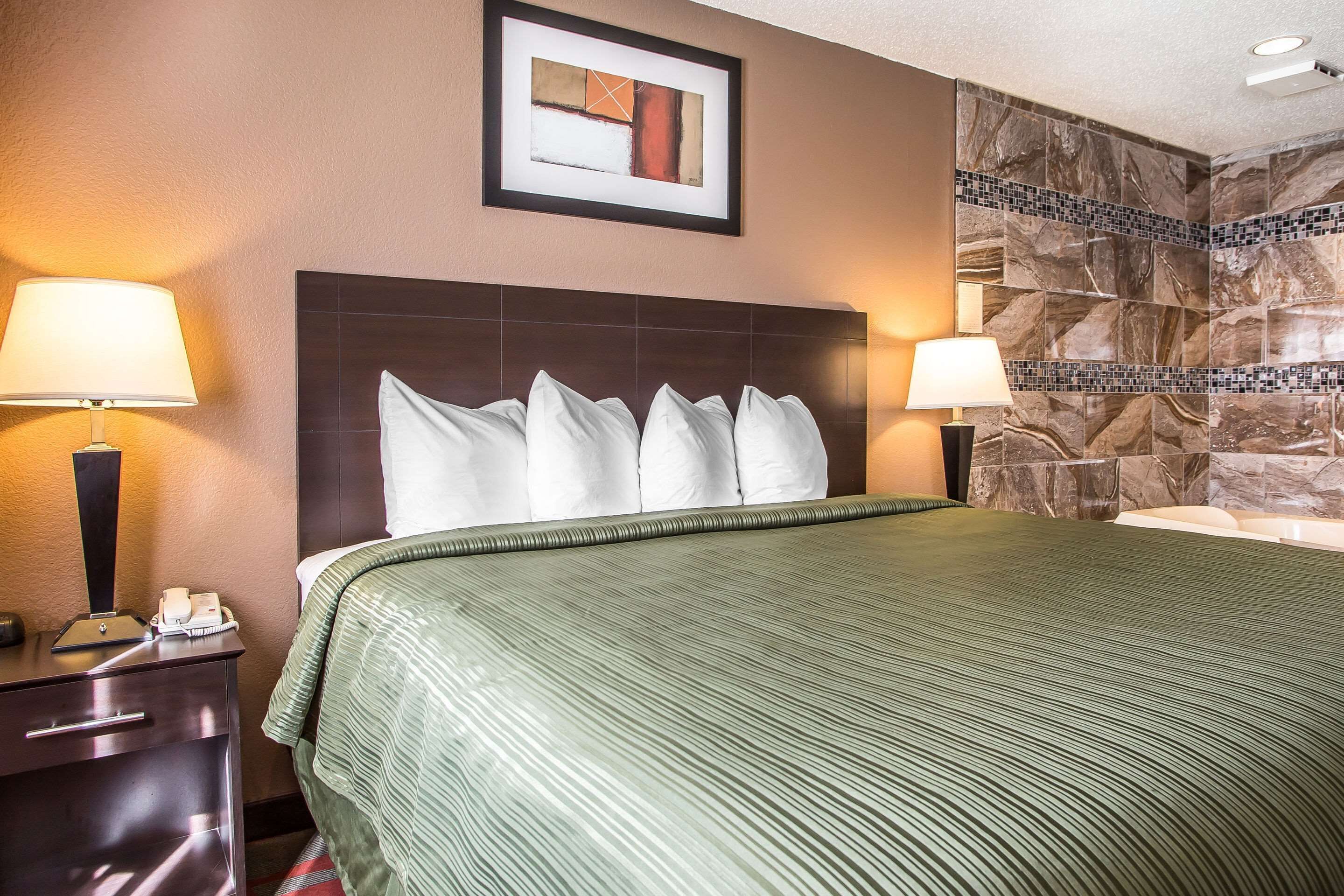A hotel room with a large bed, two bedside lamps, a framed artwork above the bed, and a stone-patterned wall.