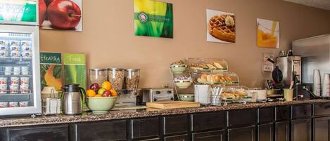 A breakfast bar with various food items, a coffee machine, and a refrigerator with beverages.