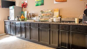 Zona de recepción de hotel con un mostrador que exhibe diversos alimentos, un refrigerador y un televisor montado en la pared.
