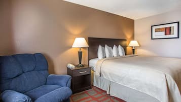 A hotel room with a bed, two bedside lamps, a nightstand with a phone, a blue armchair, and a patterned rug.