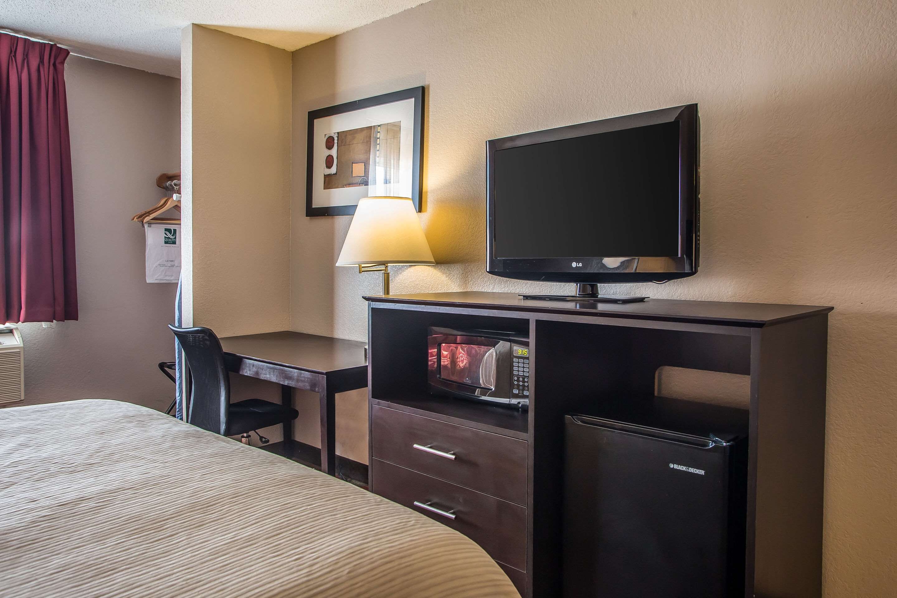 Ein Hotelzimmer mit Bett, Schreibtisch mit Lampe, Fernseher, Mikrowelle und Kühlschrank.