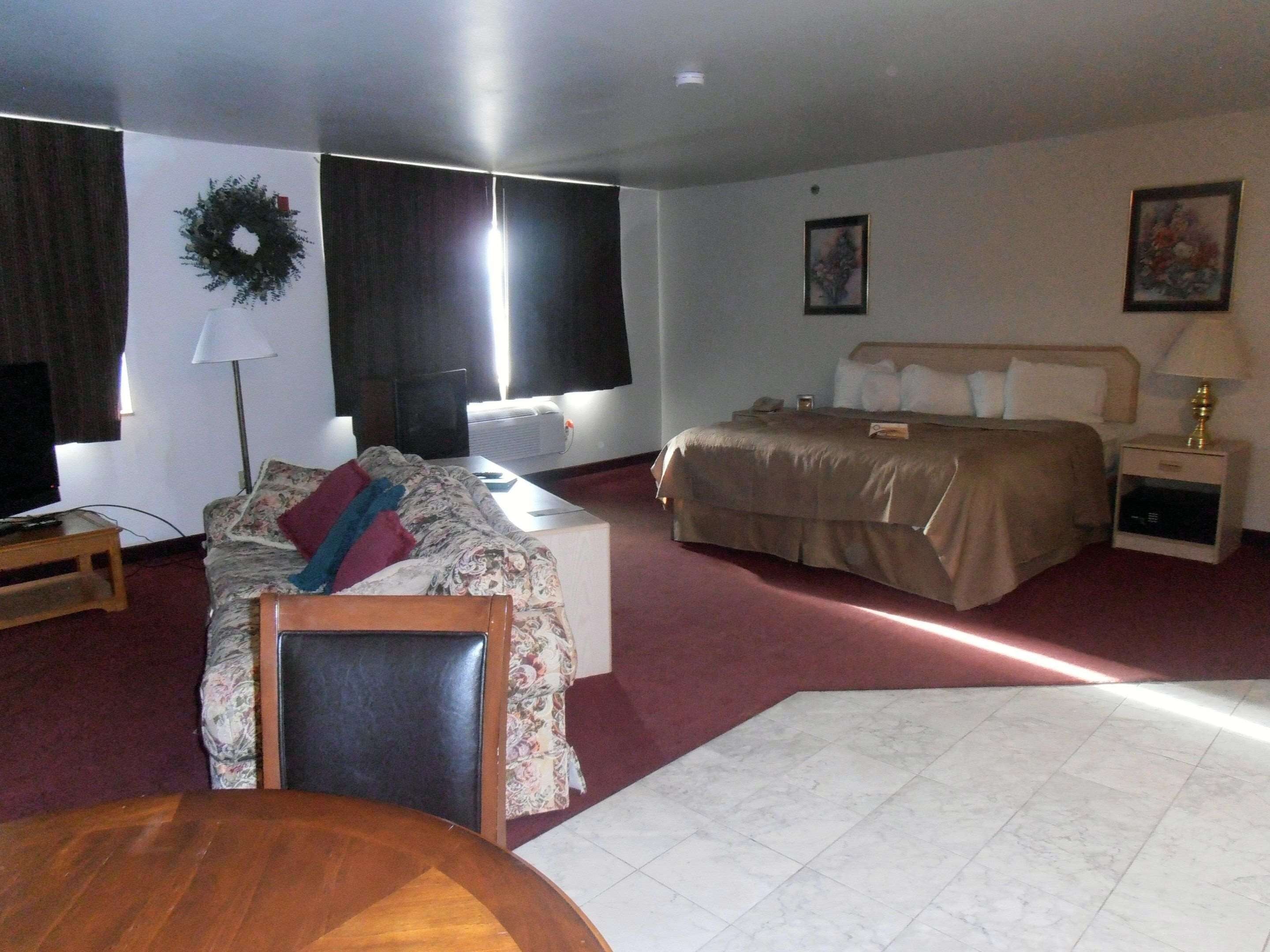 A hotel room with a bed, a desk, a chair, a TV, and a window with a wreath decoration.