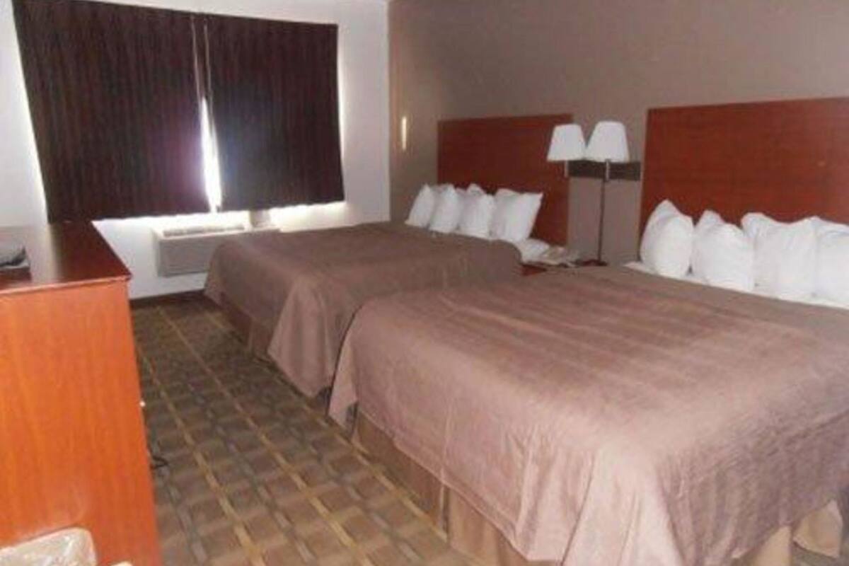 A hotel room with two beds, a desk, a lamp, and a window with curtains.