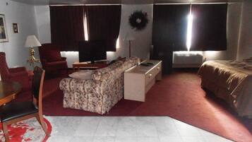 A compact living room with a sofa, a small table, a TV, and a bed.