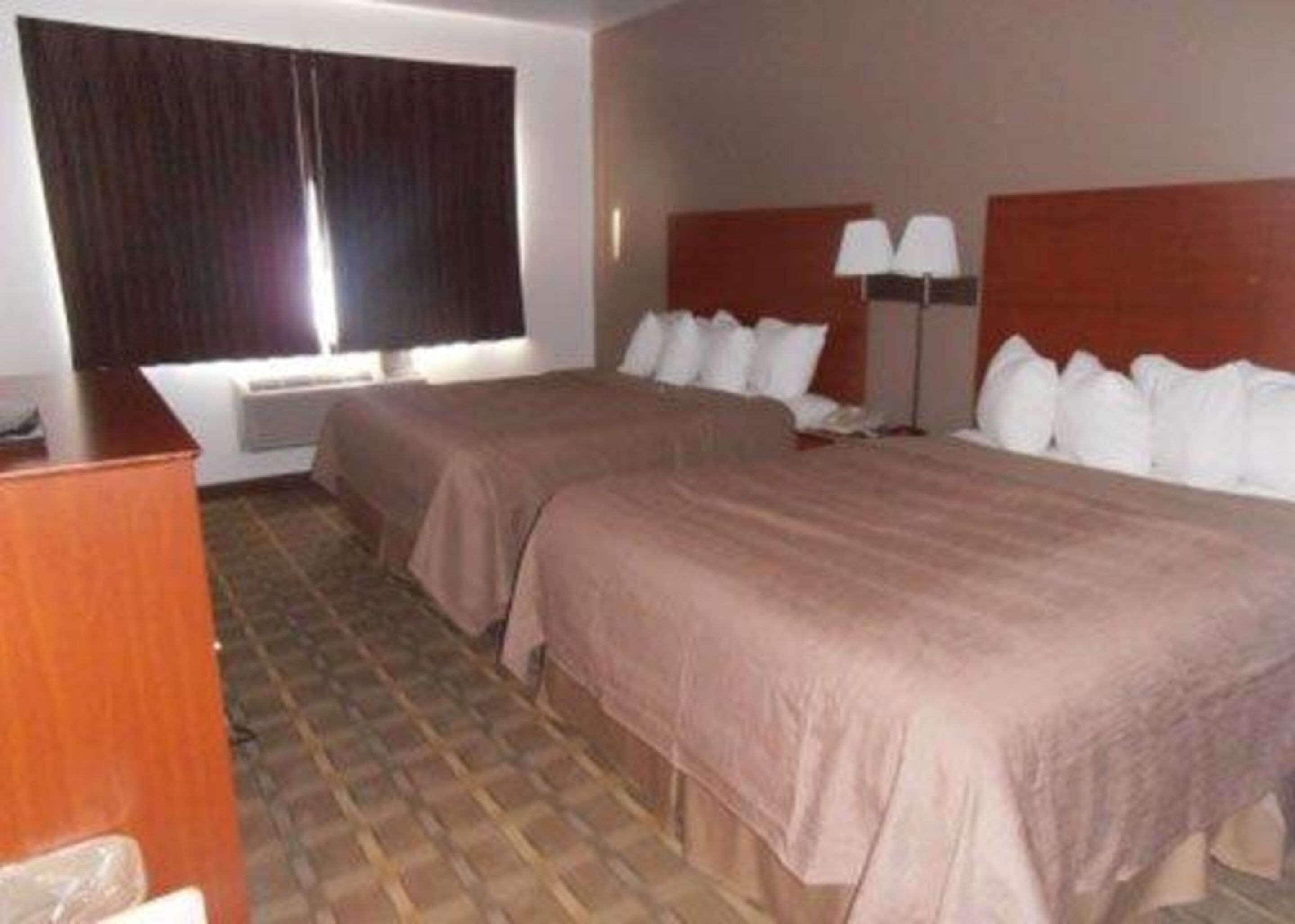 Une chambre d’hôtel avec deux lits, un bureau, une lampe et une fenêtre avec des rideaux.