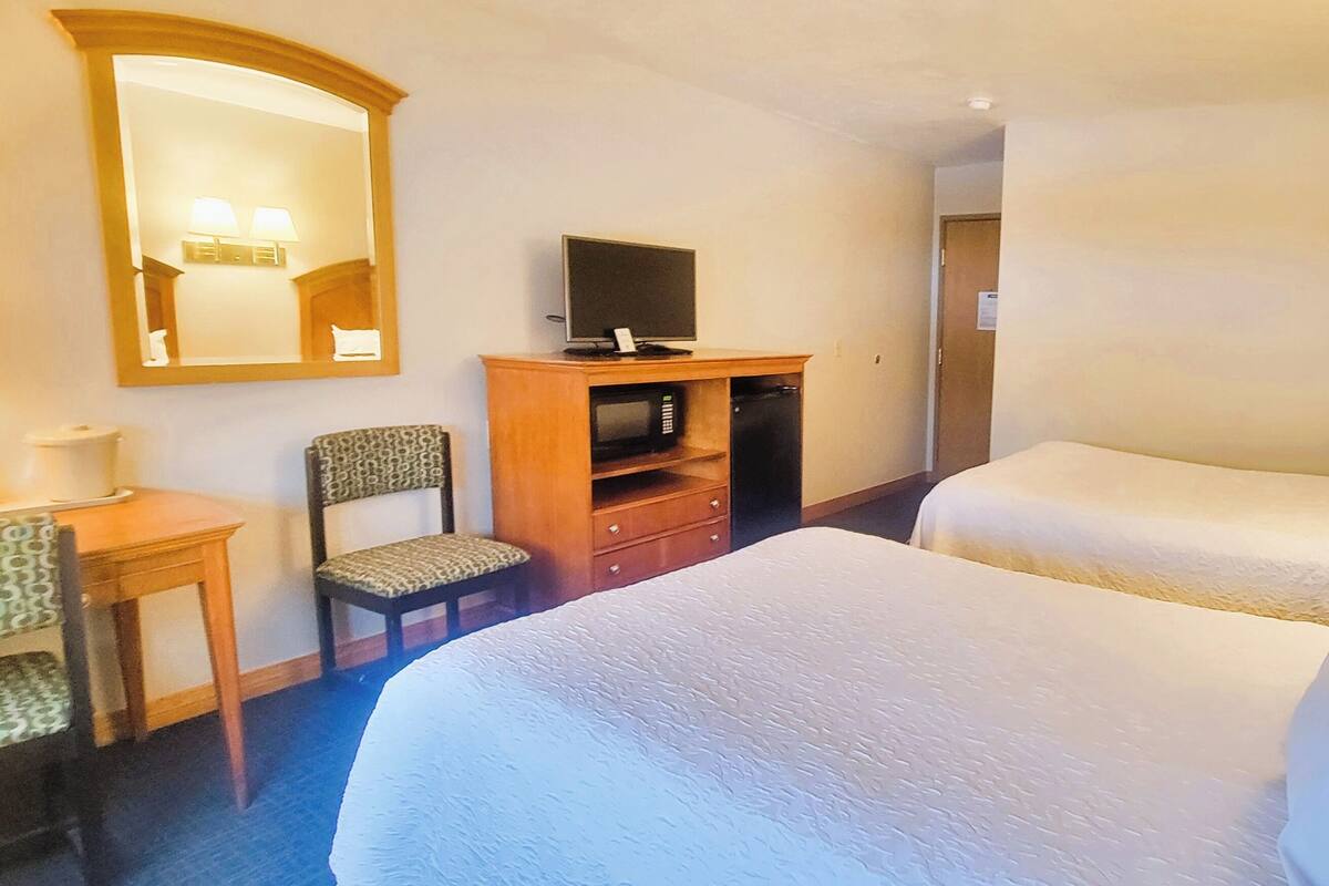 A hotel room with two beds, a desk with a chair, a television, and a microwave.