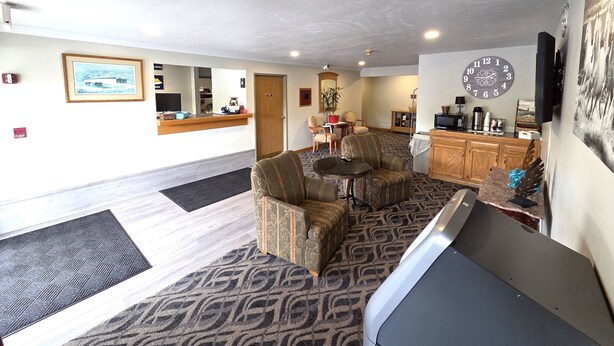 A hotel lobby with a reception desk, seating area, clock, and a large mirror. - Mountaineer Inn (Philippi)