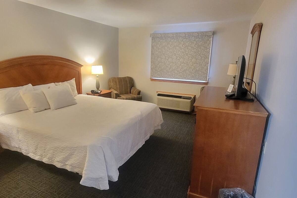 A hotel room with a large bed, bedside lamps, a chair, a desk, and a window with a curtain.