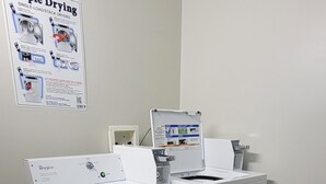A laundry area with a Whirlpool washer and dryer, a trash bin, and a poster on the wall. - Mountaineer Inn (Philippi)