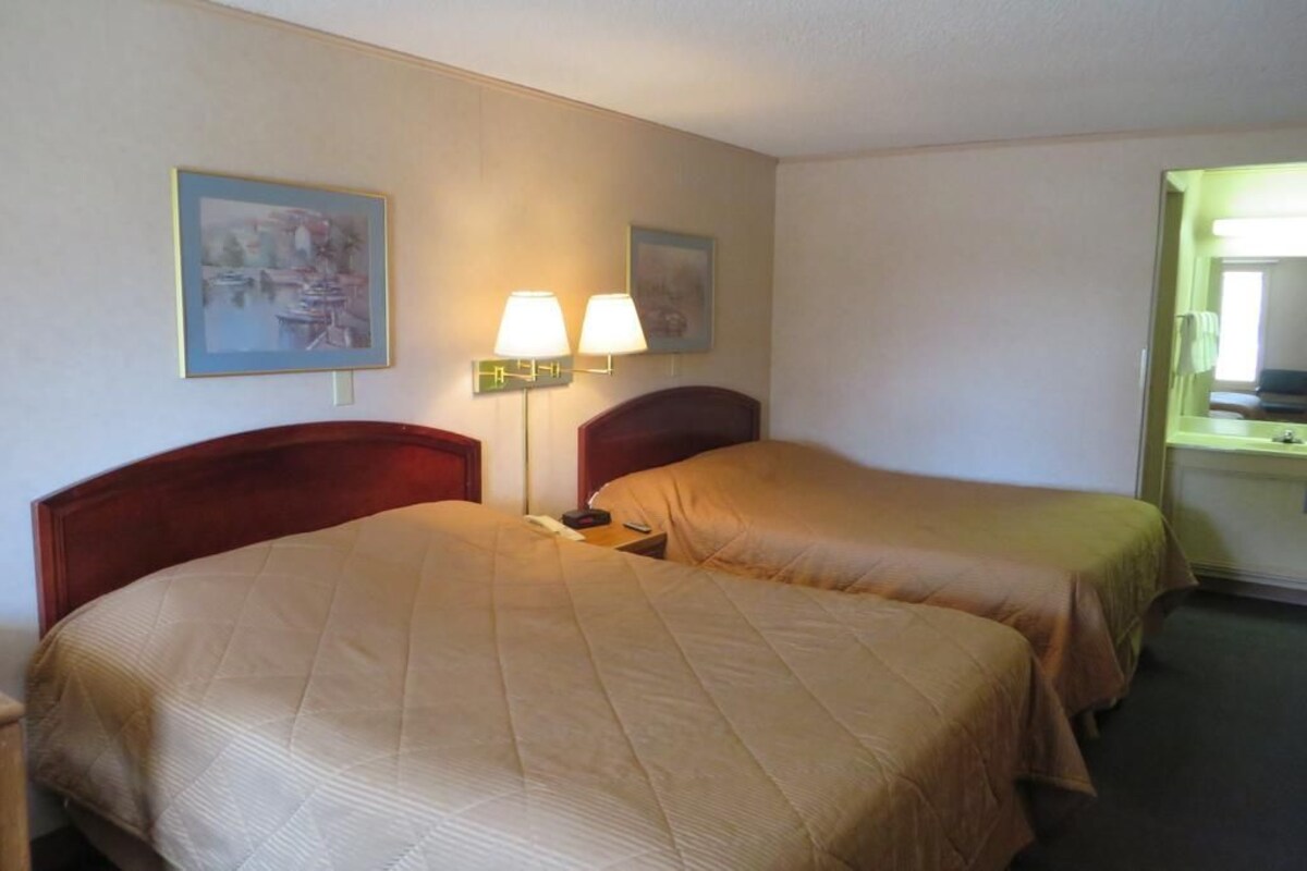Een hotelkamer met twee bedden, een nachtkastje met een lamp, en twee ingelijste foto’s aan de muur.