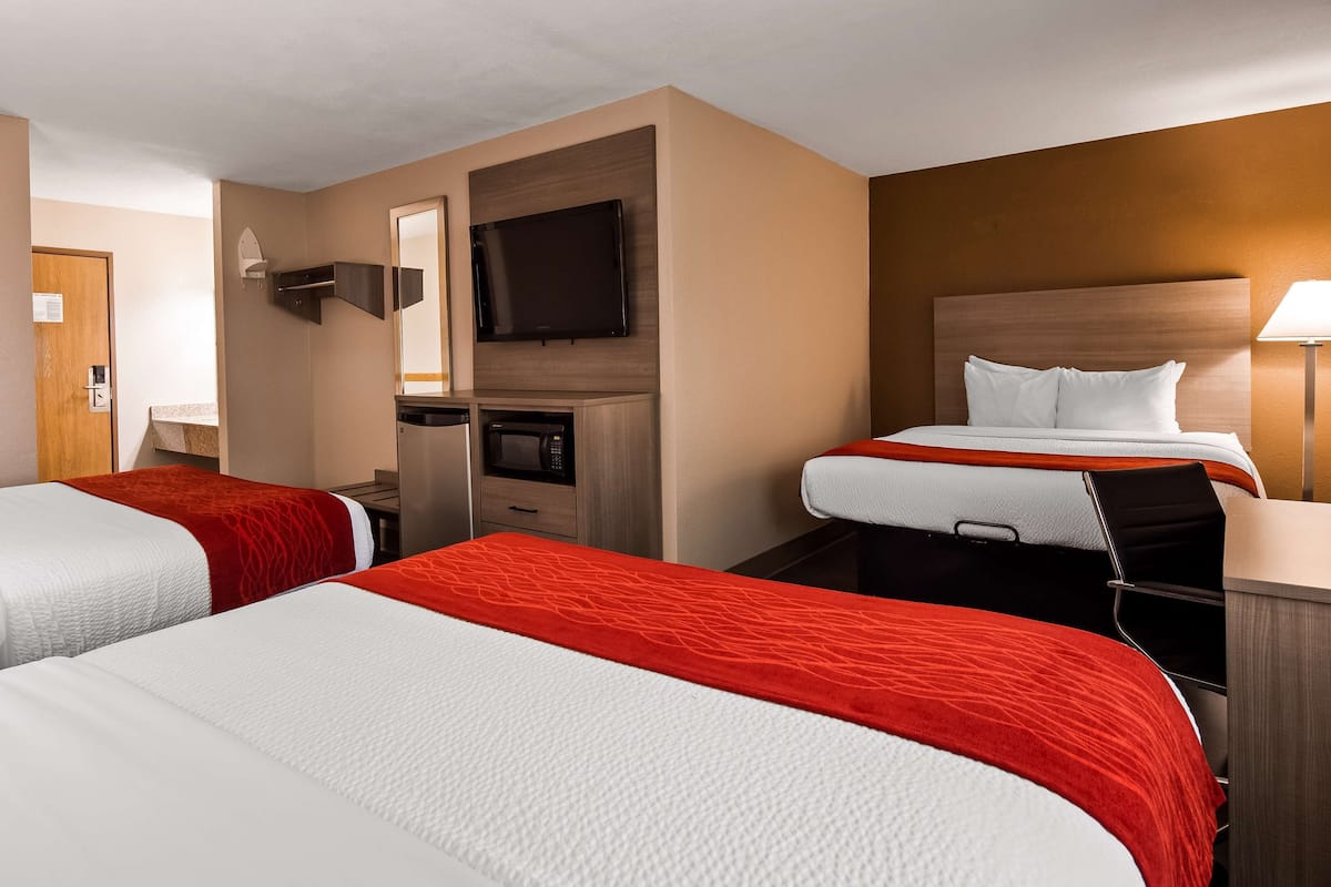 Ein Hotelzimmer mit zwei Betten, einem Fernseher, einer Mikrowelle und einem Schreibtisch mit Stuhl.