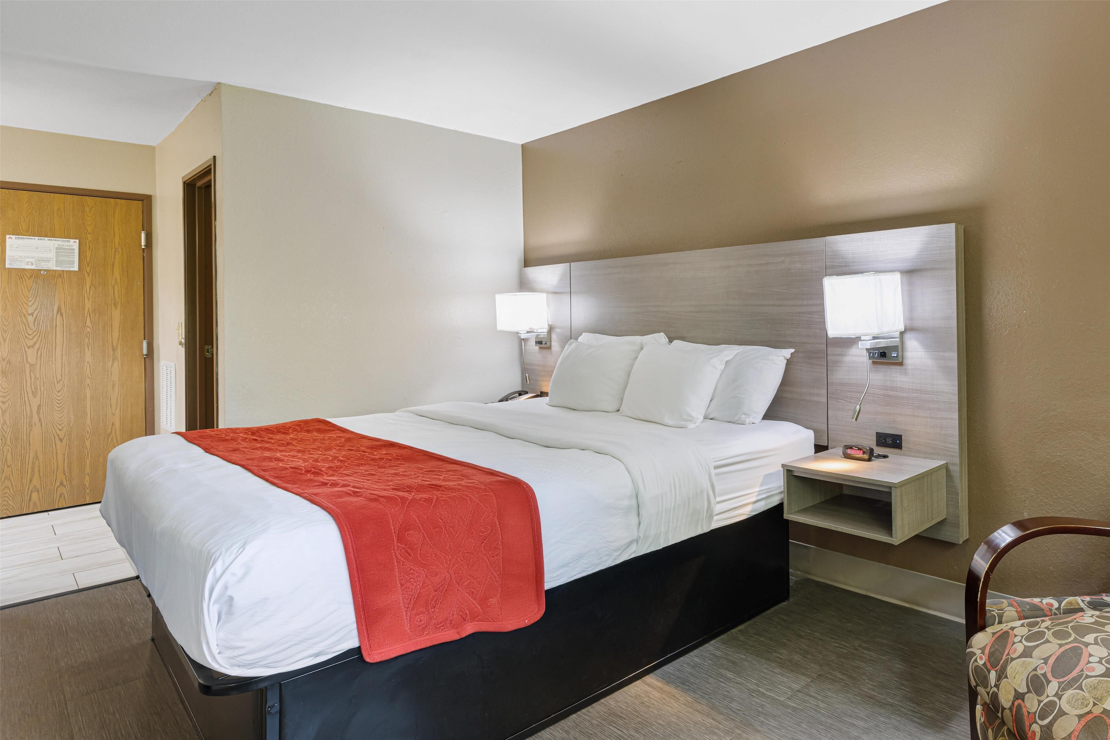 A hotel room with a bed, bedside tables, a nightstand, a chair, and a door.