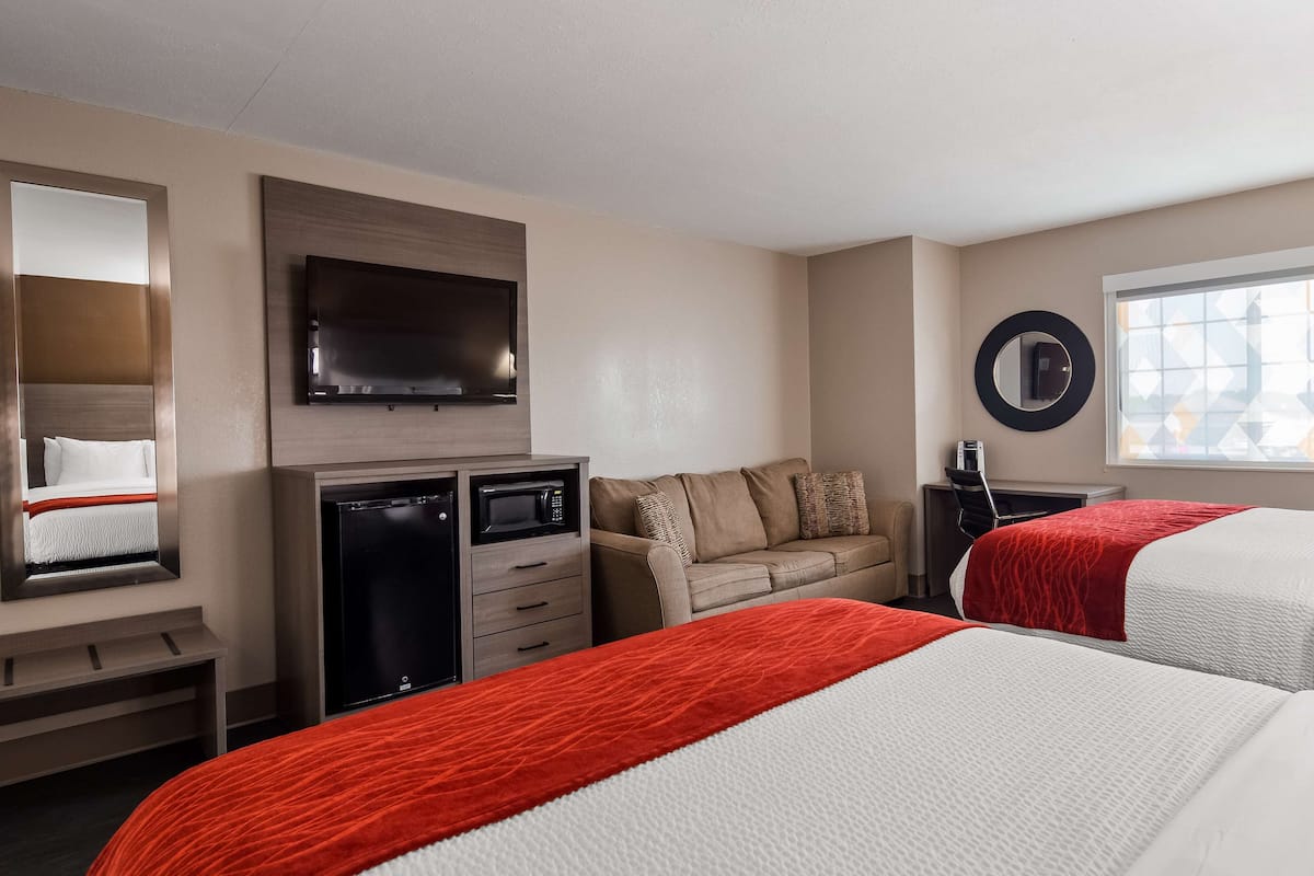 Ein Hotelzimmer mit zwei Betten, einem Schlafsofa, einem Fernseher, einem Schreibtisch mit Computer und einem Fenster.