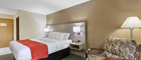 A hotel room with a bed, a nightstand, a chair, and a lamp.