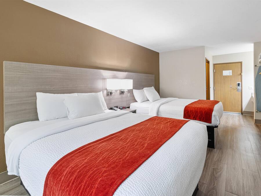 A hotel room with two beds, a wooden headboard, a red throw blanket, and a wooden floor.