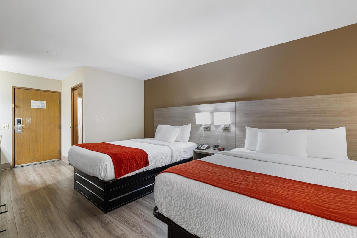 Ein Hotelzimmer mit zwei Betten, Holzboden, Holztür und einer hellen Wand.