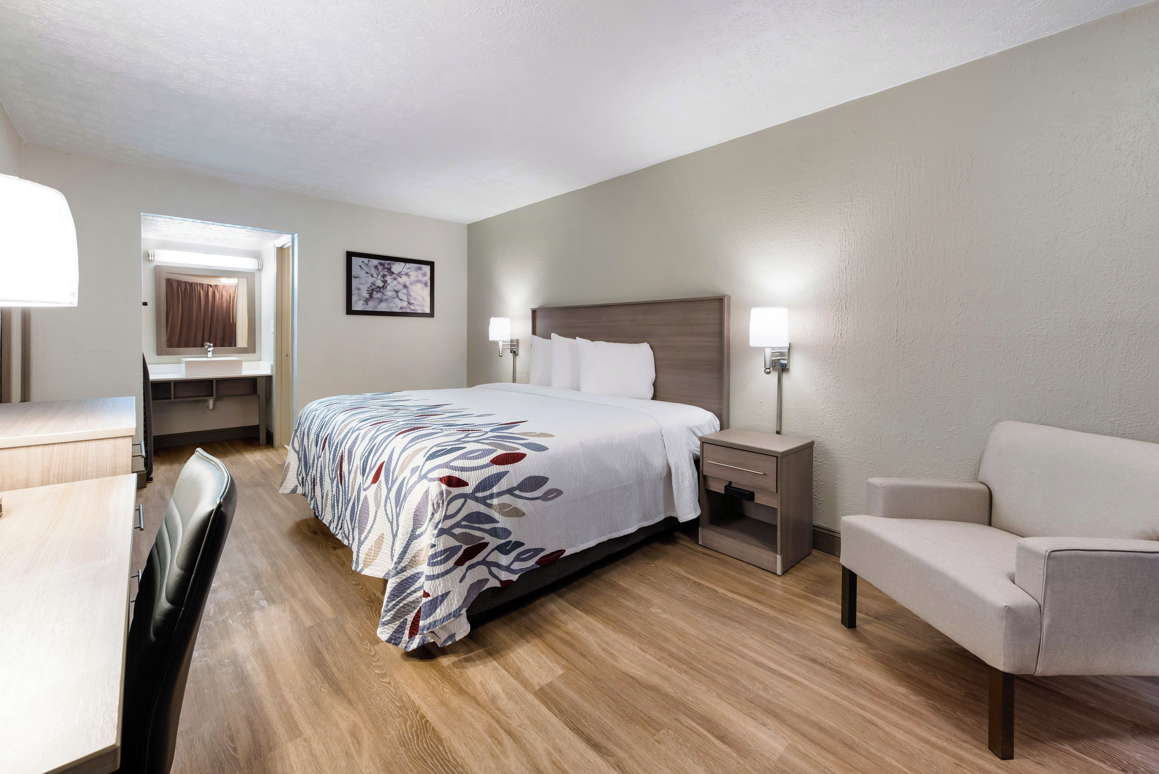 A hotel room with a bed, bedside tables, a desk, a chair, and a mirror.