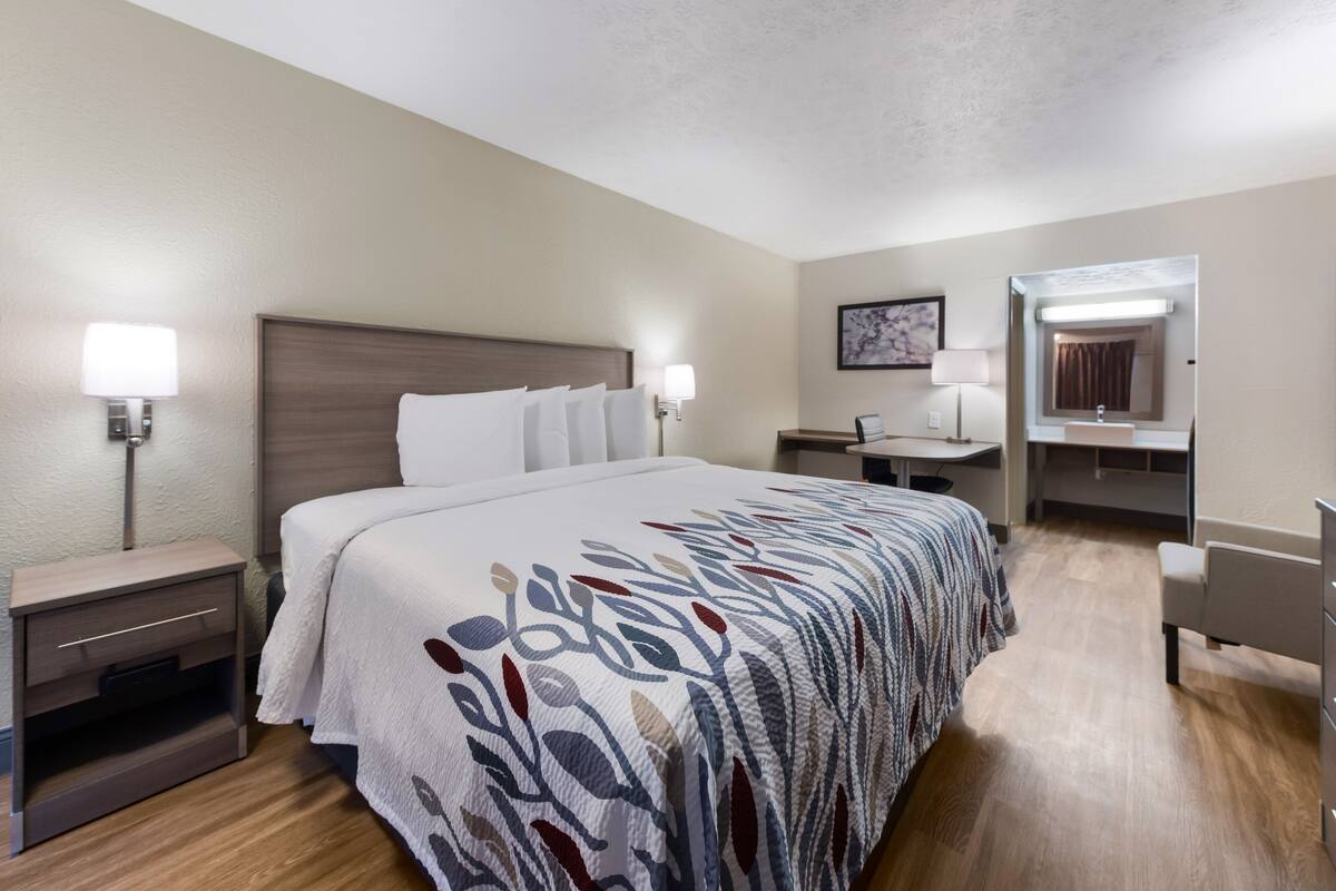 A hotel room with a large bed, bedside tables, a desk, a chair, a mirror, and a bathroom.