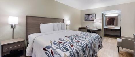 A hotel room with a bed, bedside tables, a desk, a chair, a mirror, and a wall-mounted lamp.