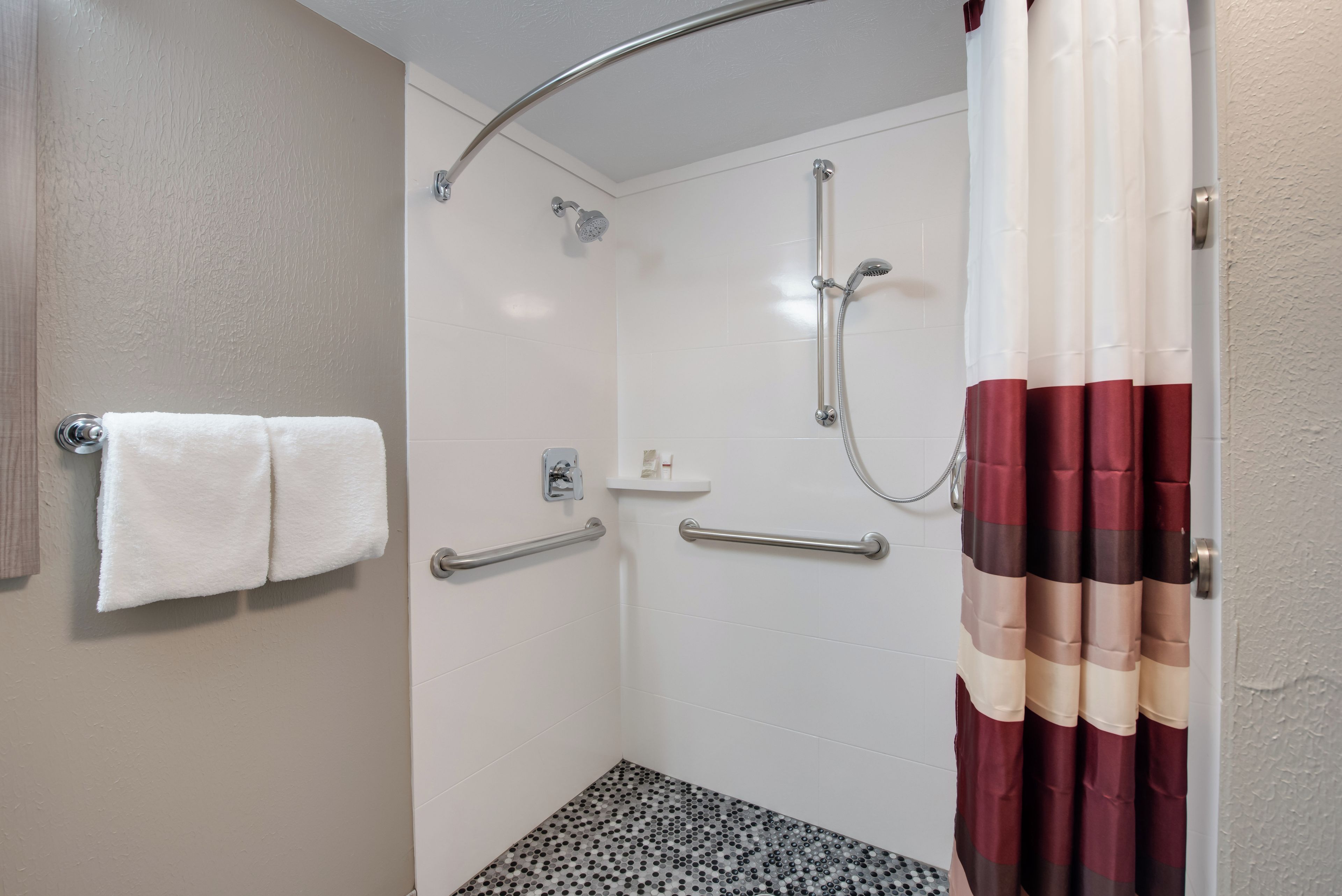 A shower area with a glass door, a handrail, and a towel rack with two towels.