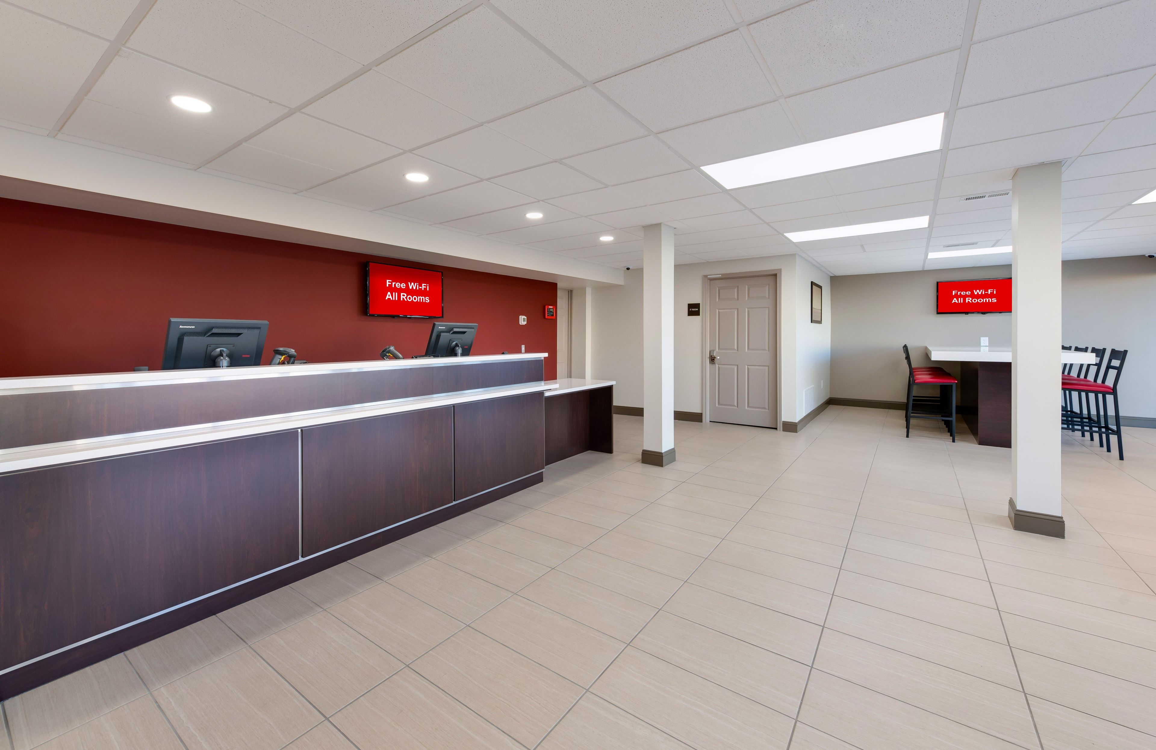 A reception area with a reception desk, a red wall, and a sign indicating free Wi-Fi in all rooms.