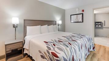 Ein Hotelzimmer mit einem Bett, Nachttischen, einer Wandleuchte, einem gerahmten Bild und einem durch eine offene Tür einsehbaren Badezimmer.
