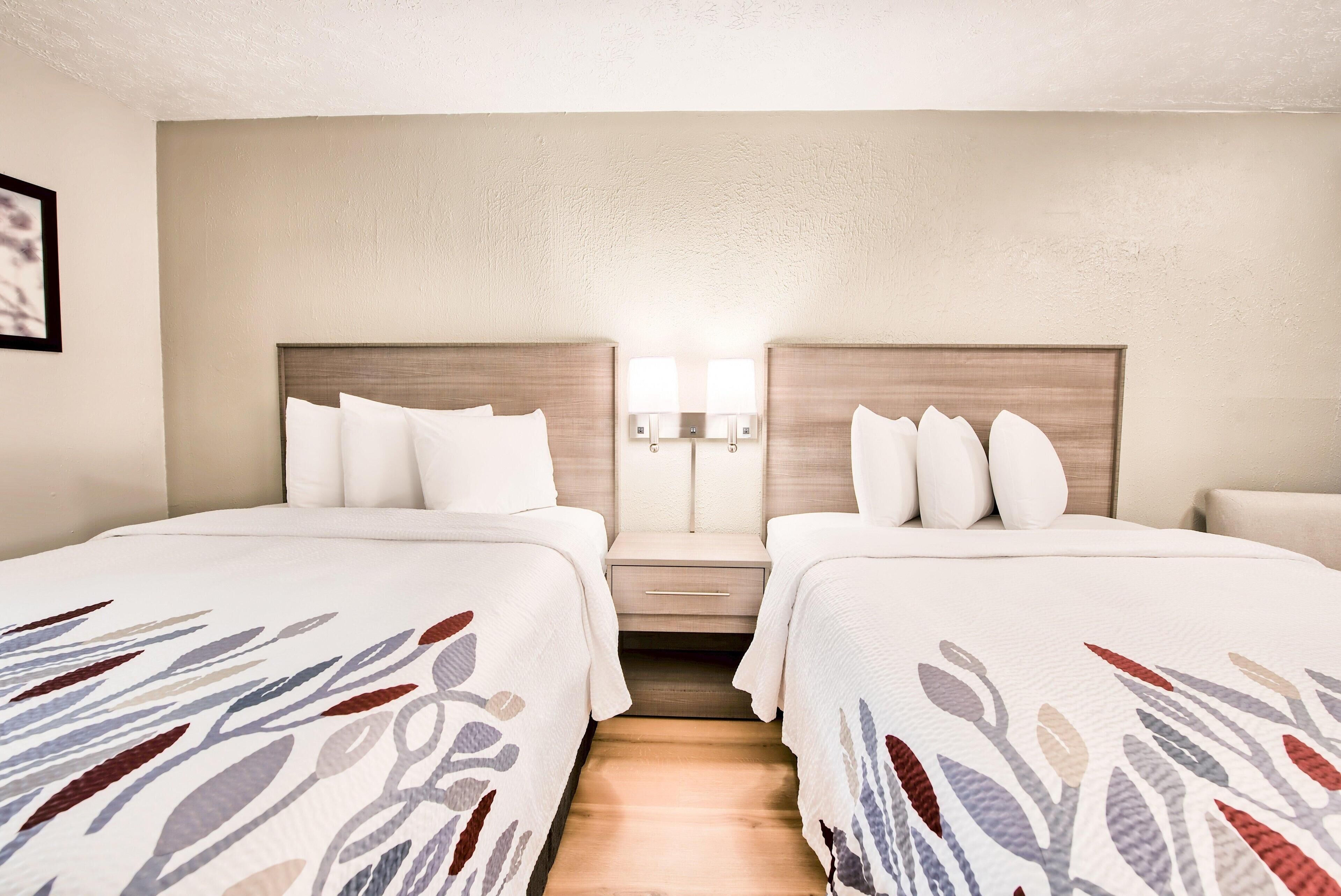 A hotel room with two beds, a nightstand, and two wall-mounted lamps.