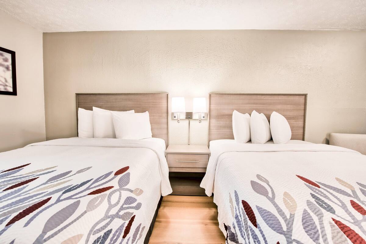A hotel room with two beds, a nightstand, and two wall-mounted lamps.