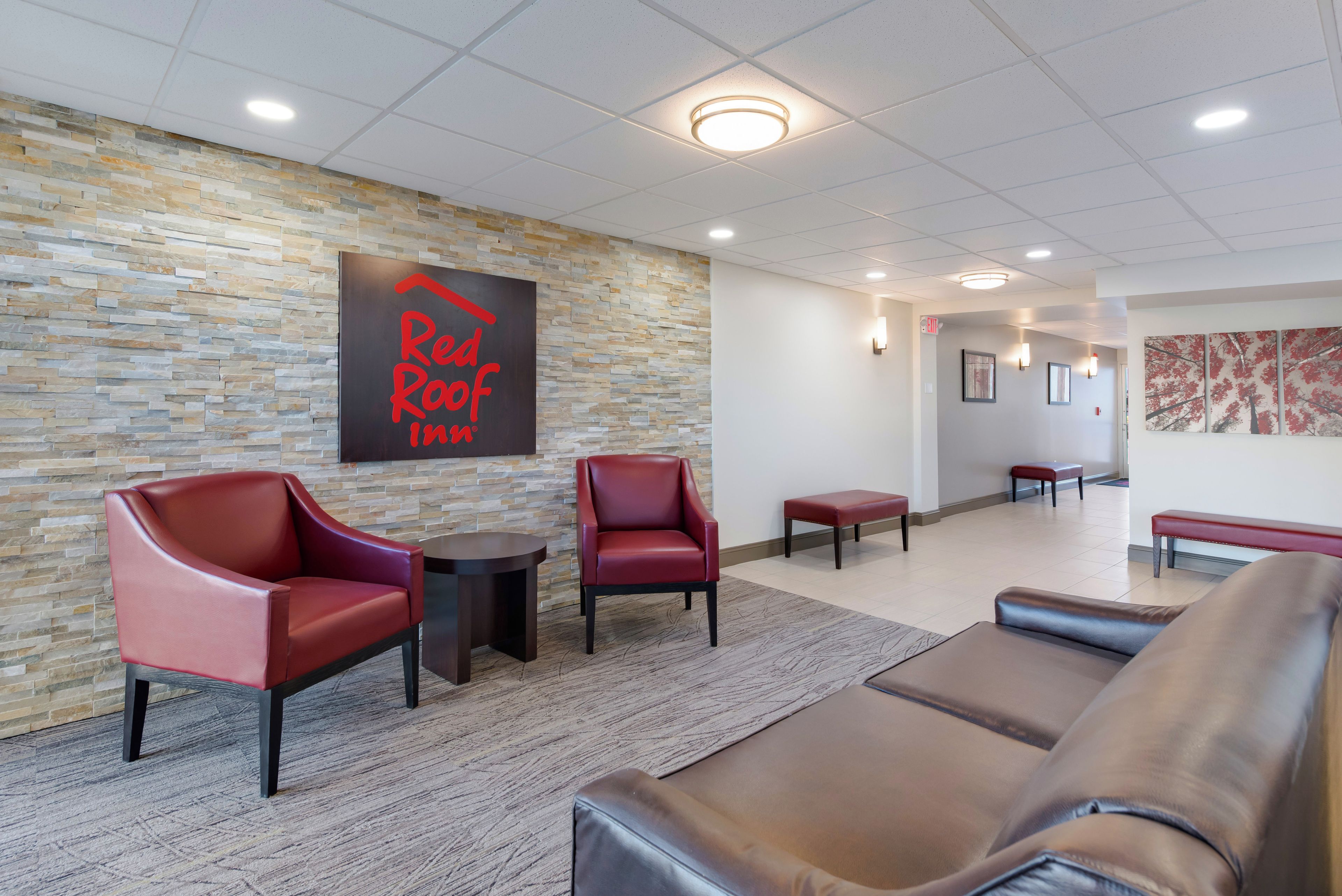 A lobby with stone walls, a Red Roof Inn sign, leather seating, and a tiled floor.