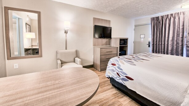 A hotel room with a bed, a desk, a chair, a TV, a dresser, and a mirror.