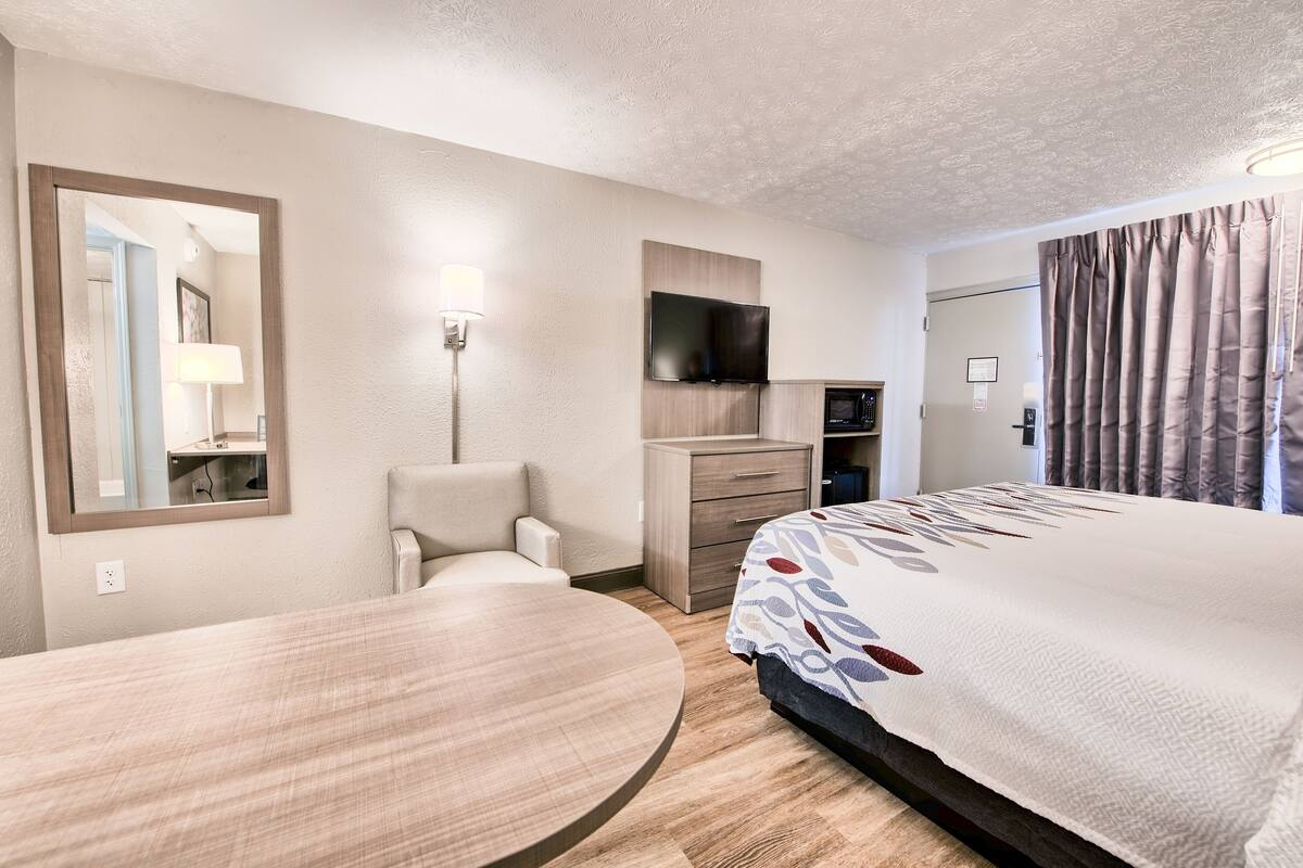 A hotel room with a bed, a desk, a chair, a TV, a dresser, and a mirror.