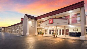 A Red Roof Inn with a two-story structure, a parking lot, and a sunset sky.
