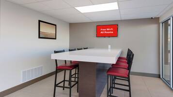 A conference room with a long table, red chairs, a framed picture on the wall, and a sign indicating free Wi-Fi.