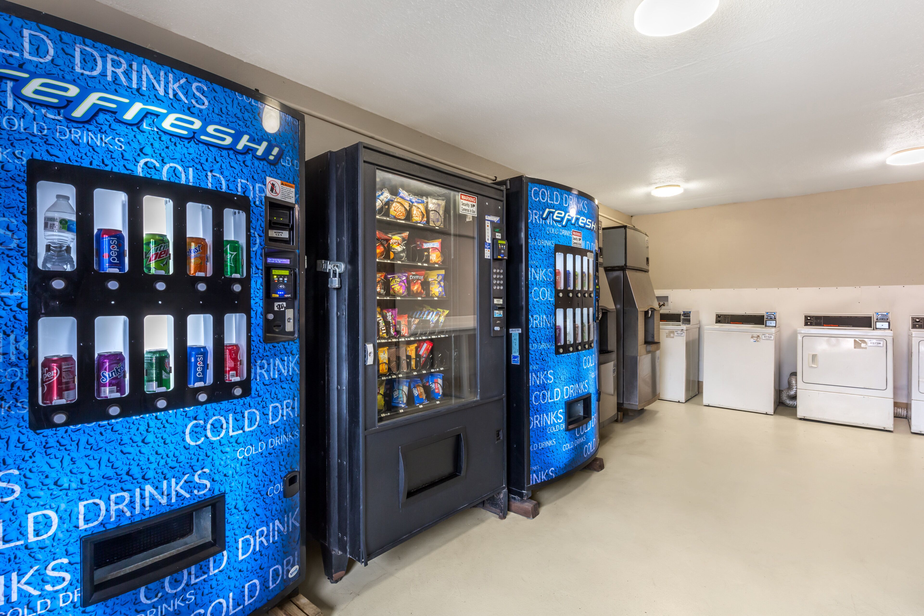 A row of vending machines in a room with a plain wall and a ceiling light.