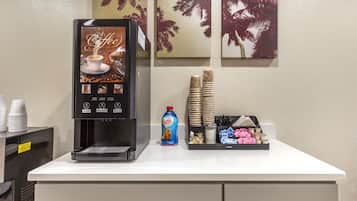 A coffee machine with a beverage selection panel, disposable cups, a bottle of coffee mate, and a tray with utensils and condiments.