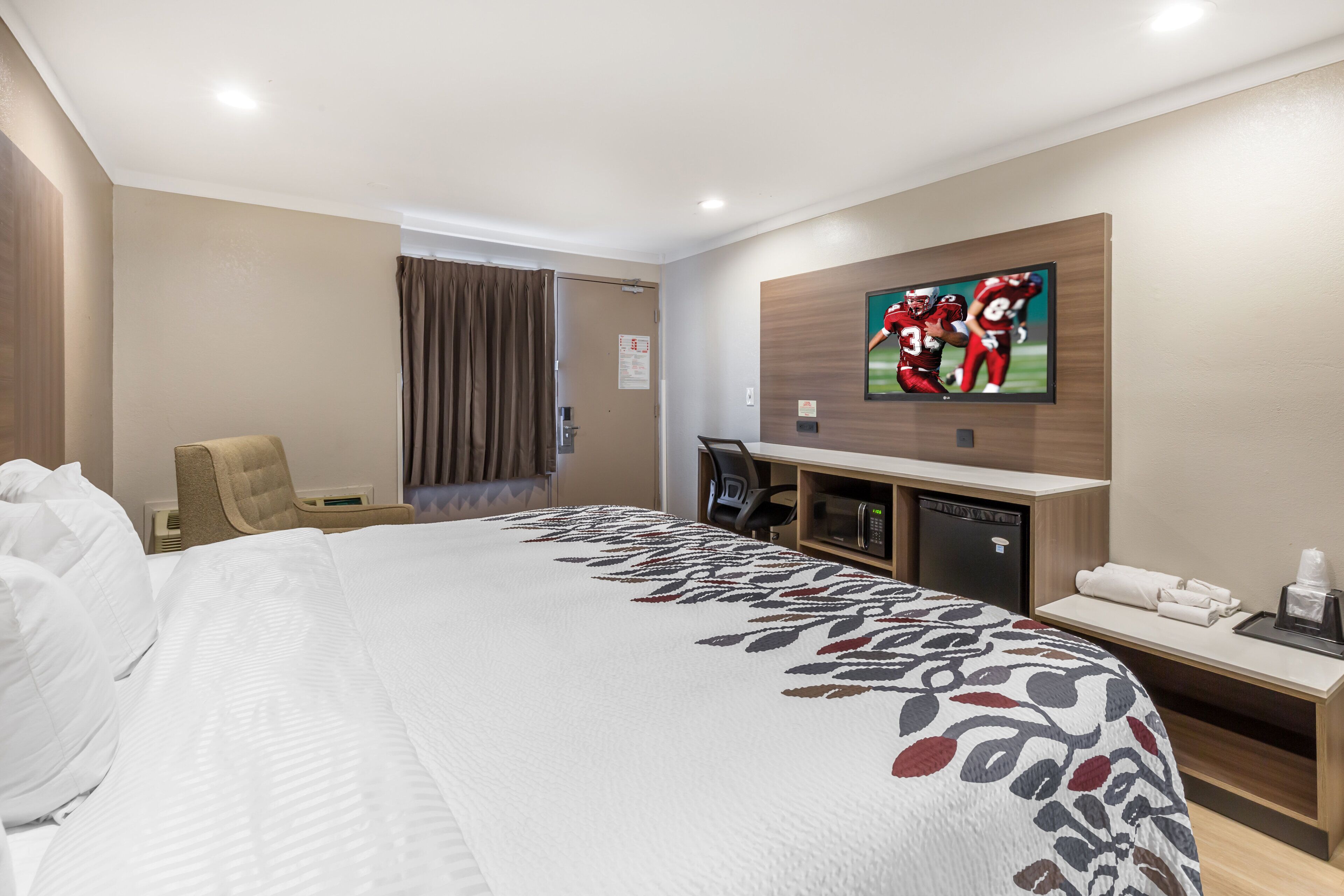 A hotel room with a large bed, a desk with a computer, a television, and a minibar.